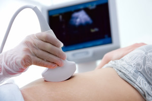 woman getting ultrasound diagnostic from doctor, close up of doctor's gloved hand with ultrasound monitor in the background